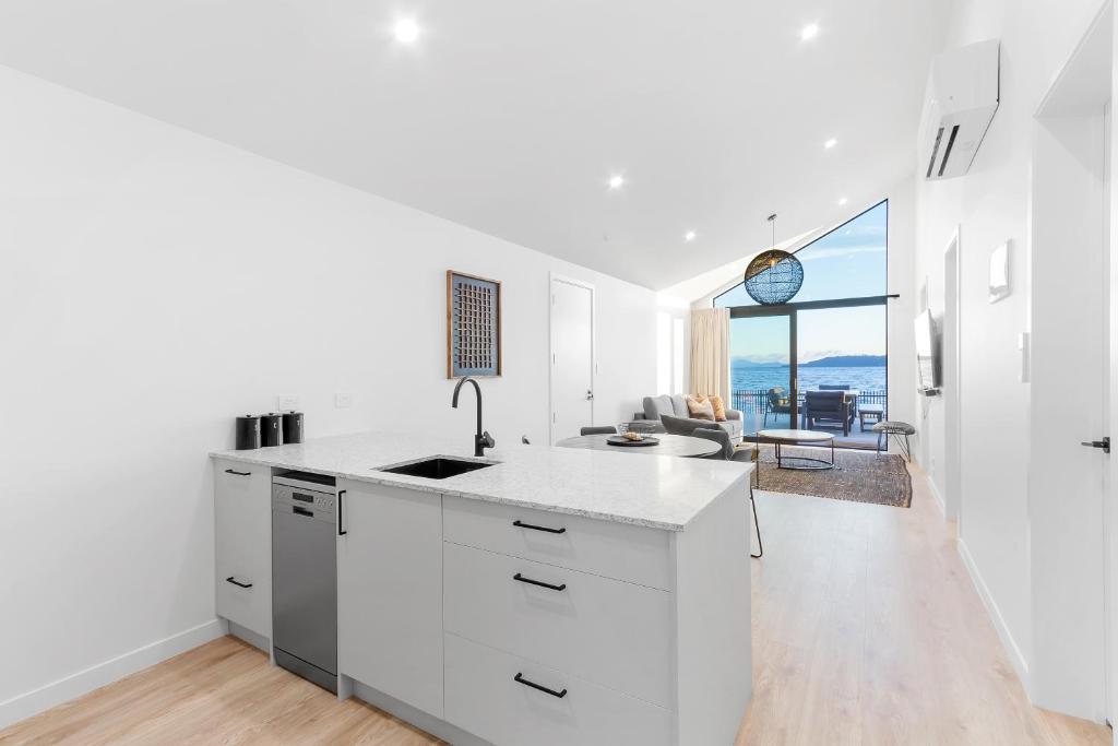 a kitchen with white cabinets and a living room at Absolute Lakefront House in Taupo