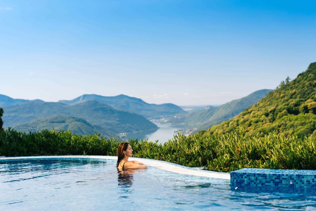 una donna seduta in una piscina con montagne sullo sfondo di Kurhaus Cademario Hotel & SPA - Adults Only a Cademario