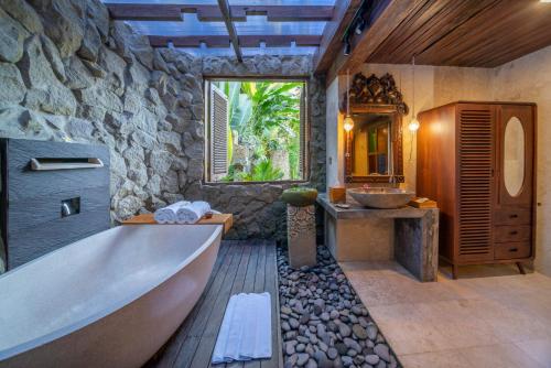 ウブドにあるMenzel Ubudの浴槽と石の壁のあるバスルーム